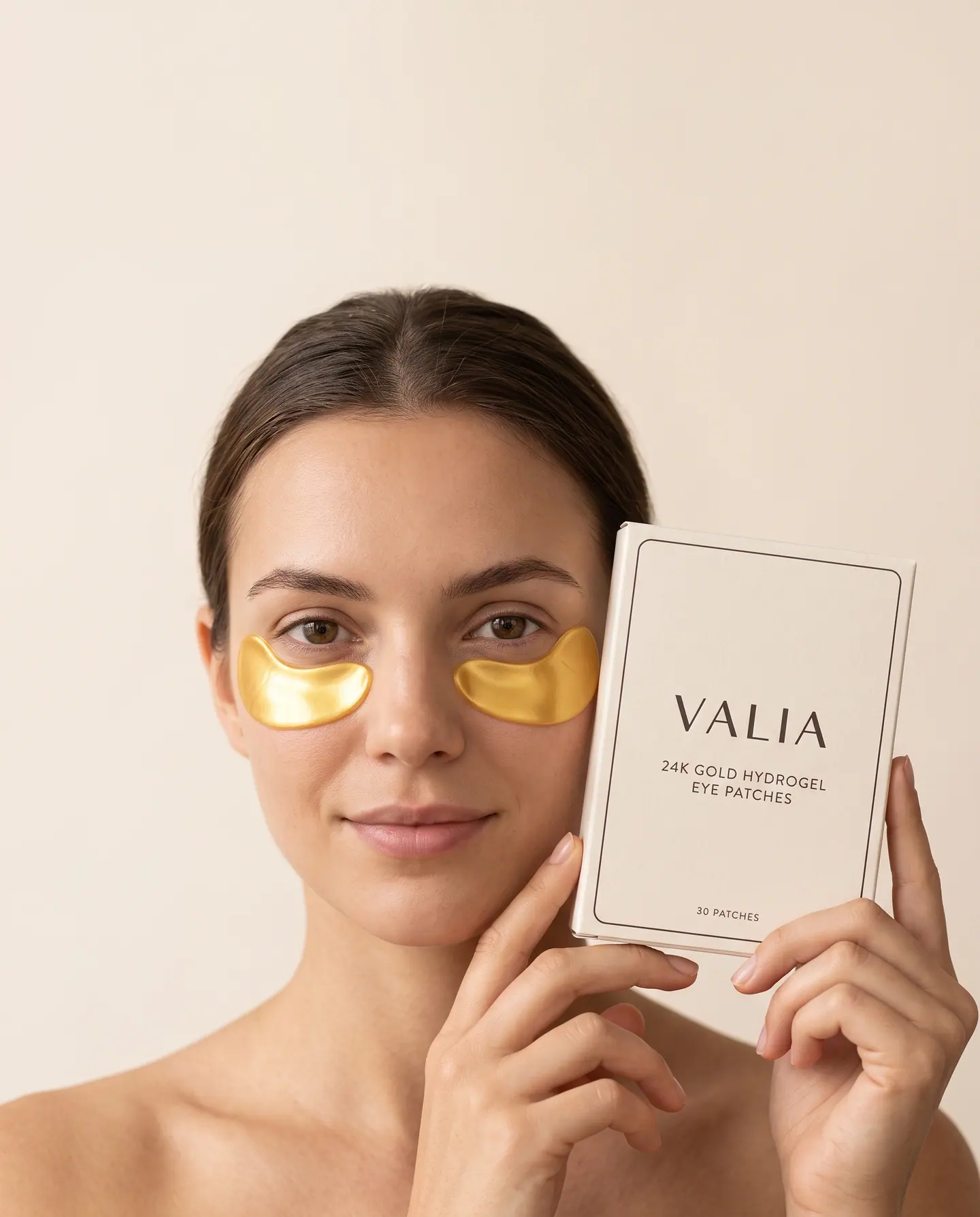 A woman holding the VALIA box, gold hydrogel crescents under each eye.